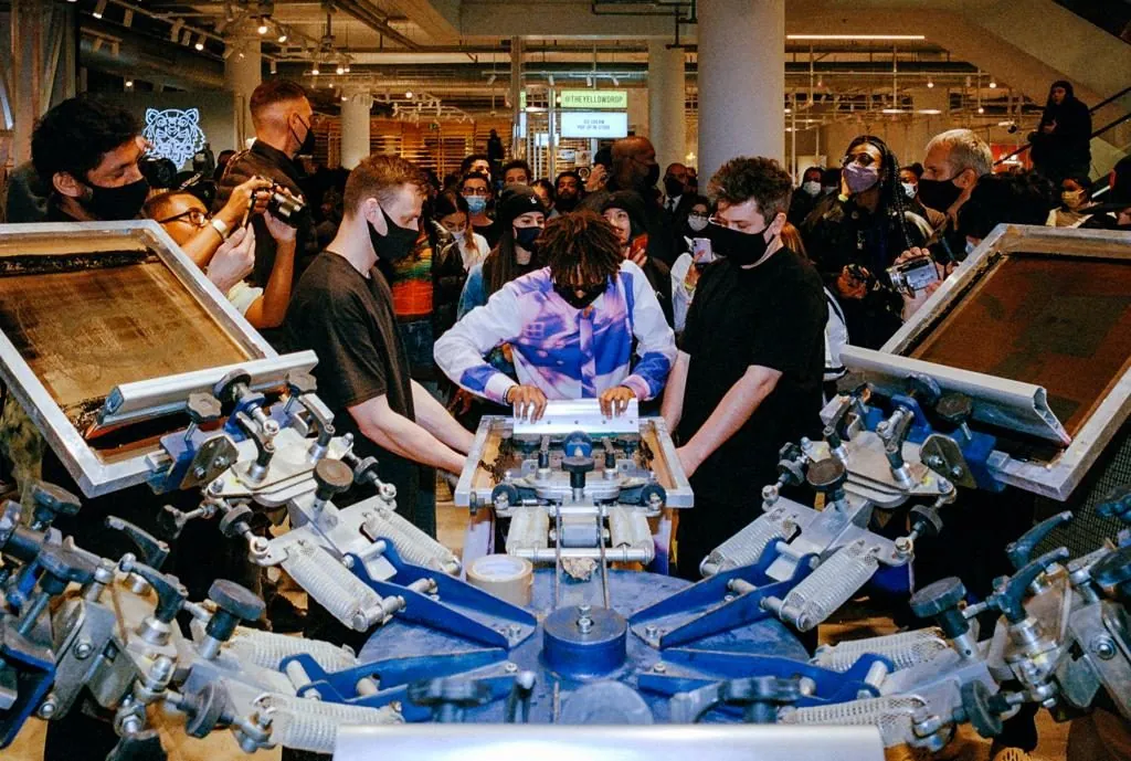 Screen printing press mid-run at Selfridges Manchester, crowd gathered around the carousel.