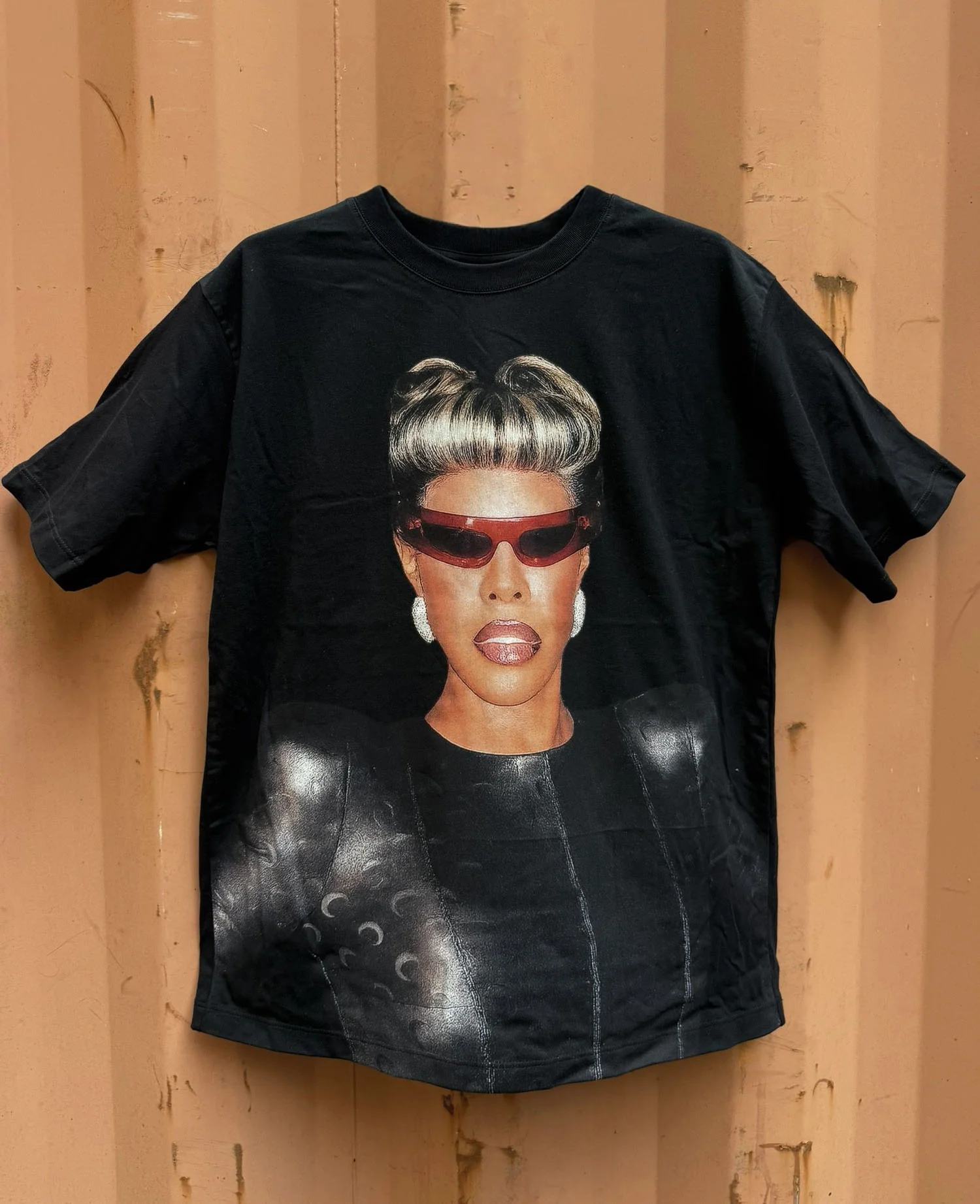 Black oversized cut & sew tee with a full-front photographic portrait print for Honey Dijon's The Nightlife, hung against a rust-orange shipping container