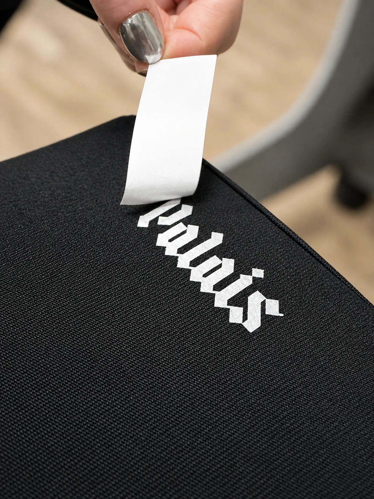 Screen printed transfer backing being removed from a metallic Palais label on heavyweight black garment